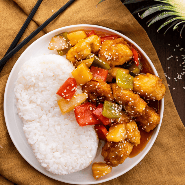 chicken and veggies in sauce with rice on white plate