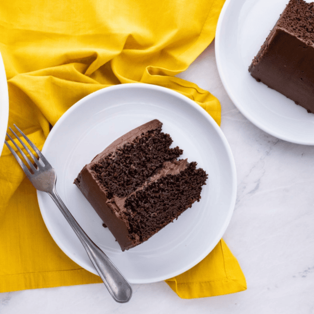 piece of cake on a white plate with a fork. other plate on side served on decorated table