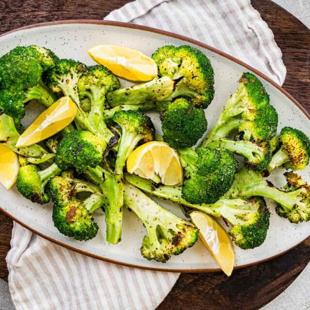 Grilled vegetables on serving plate with lemon wedges.