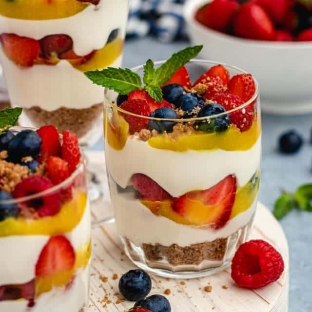 Cheesecake Parfaits layered parfaits in small glasses on tray. berries and mint leaves as decoration on tray. side view, 1x1